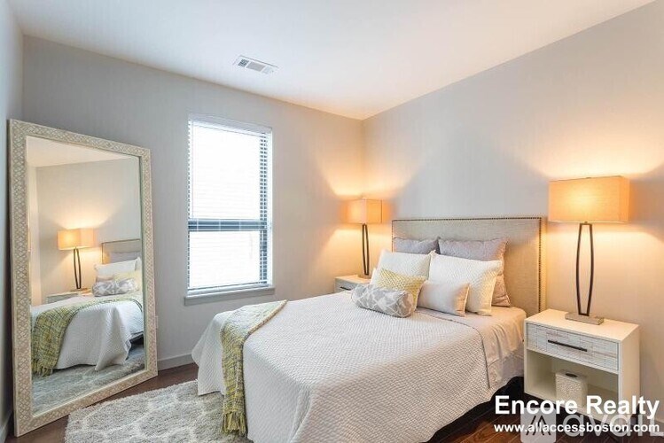 A bedroom with a large bed, a mirror, and two lamps.