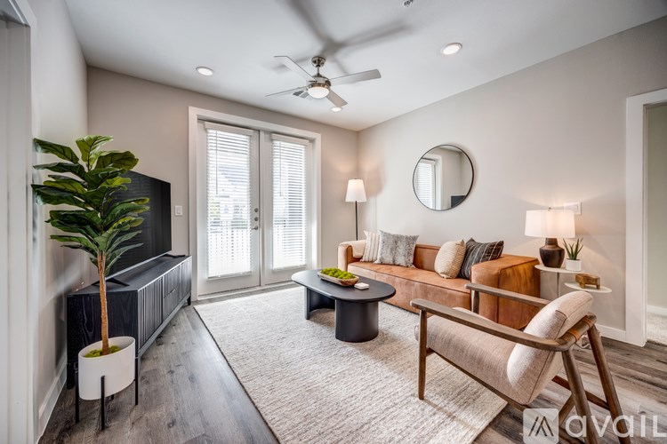 A living room with a brown sofa, a black coffee table, a plant in a white pot, and a round mirror on the wall.