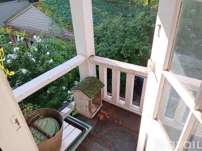 A birdhouse sits on a porch next to a trash can.