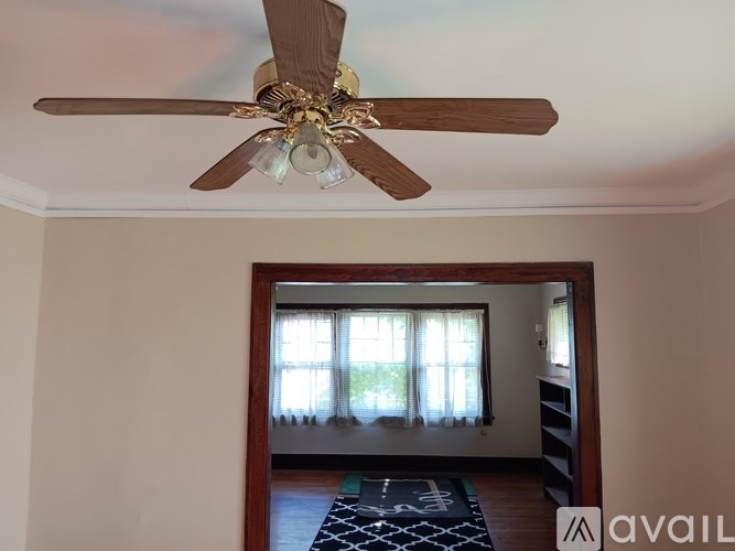 A room with a ceiling fan and a view of a window with curtains.