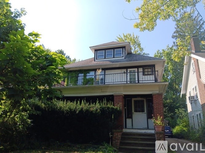 A house with a balcony and a white door is surrounded by greenery.
