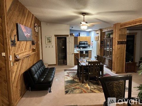 A living room with a black leather couch and a wooden wall.