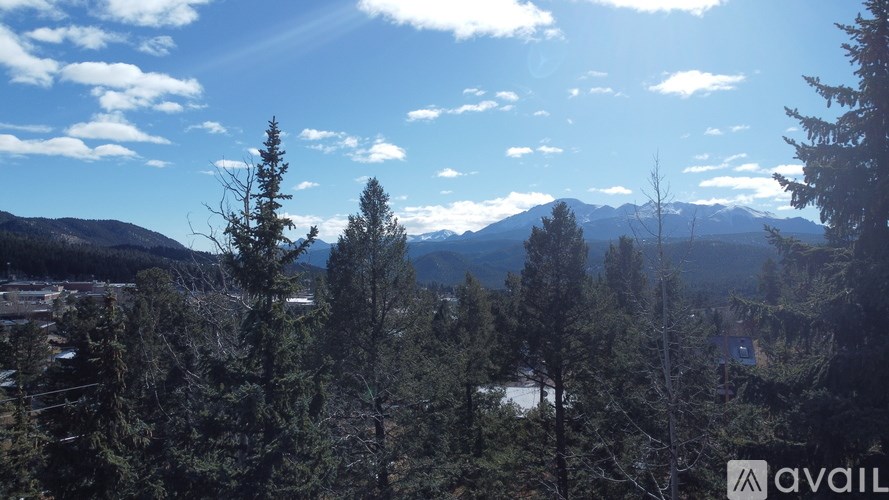 A mountain range with trees in the foreground and a partly cloudy sky.