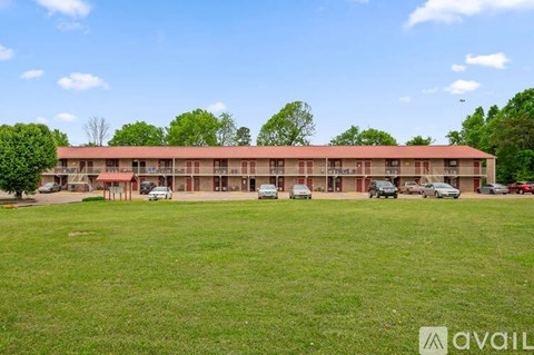 A building with a grassy field in front and cars parked in front of it.