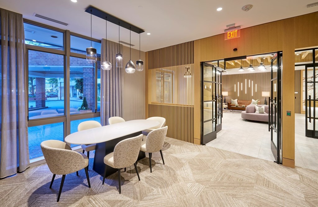 A conference room with a long table and chairs, a carpeted floor, and a view of the outside through the windows.