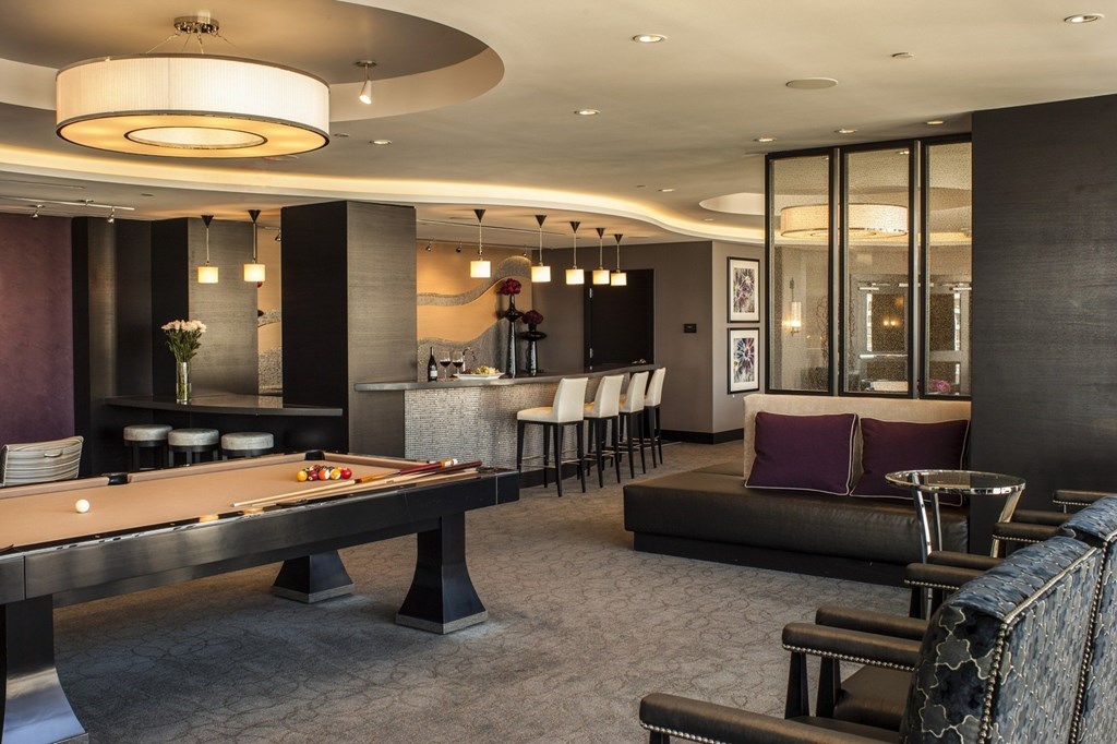A billiard table is in the middle of a room with a bar and a couch.