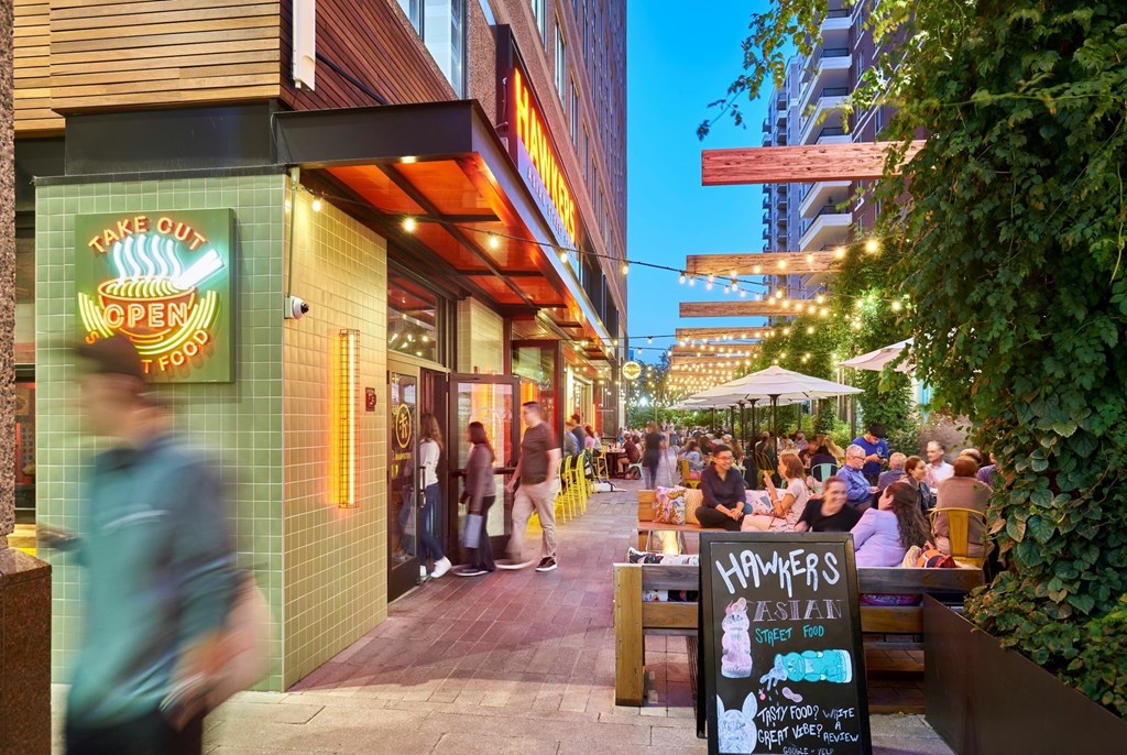 A busy street with people walking and sitting at tables outside a restaurant.