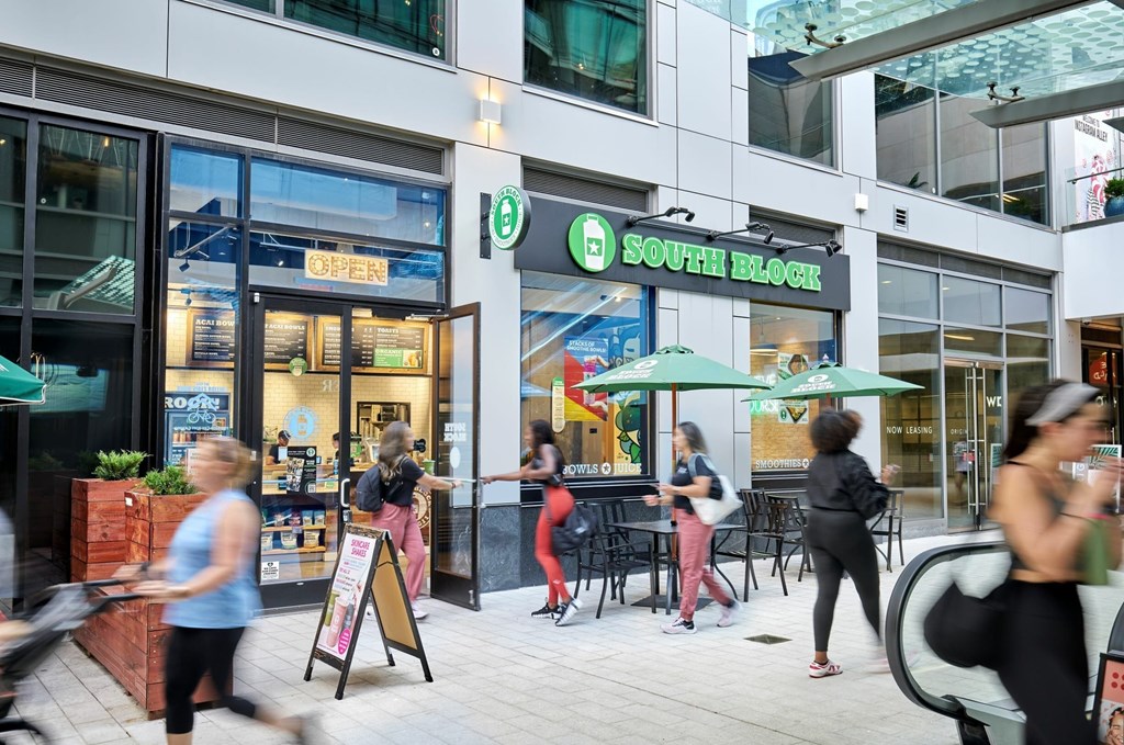 A group of people are walking in front of a store with a green awning.