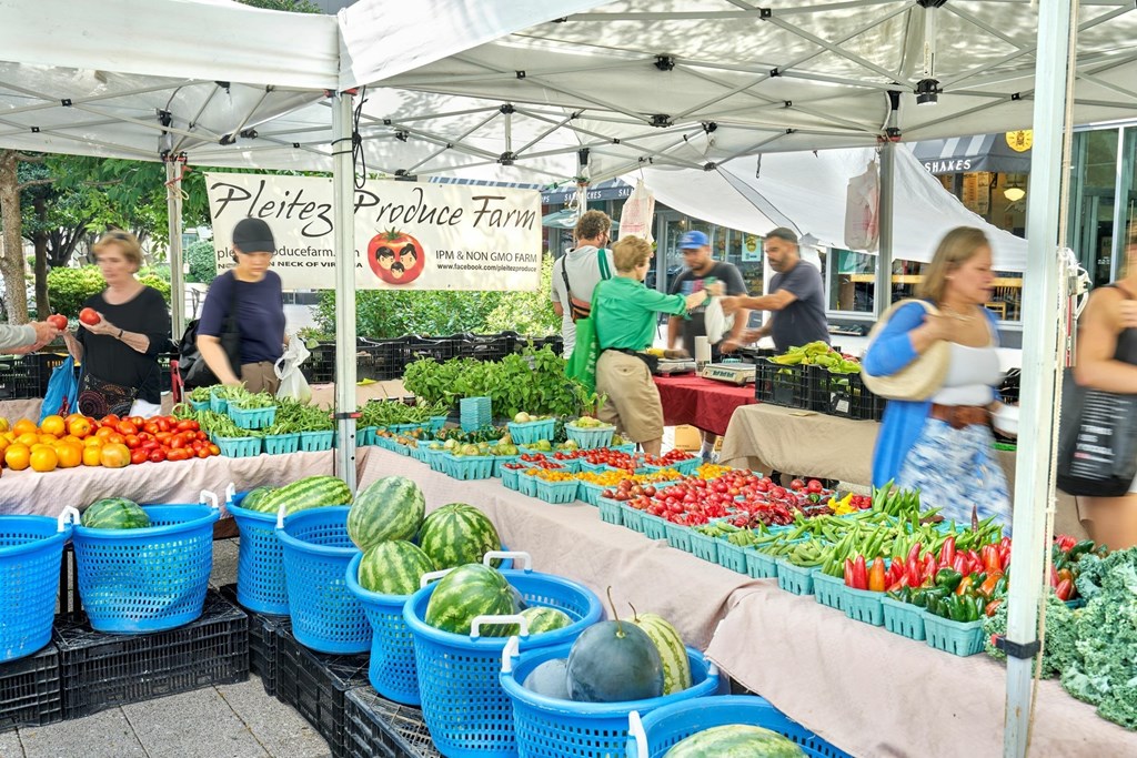 A produce farm stand with people shopping for vegetables.