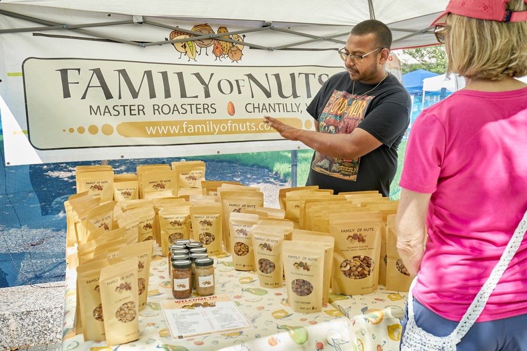 A man is standing behind a table with bags of nuts and jars of nut butter.