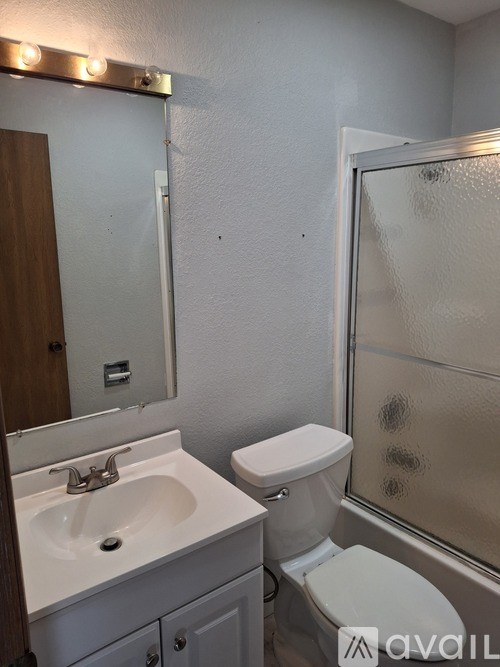 A bathroom with a toilet, sink, mirror and shower.