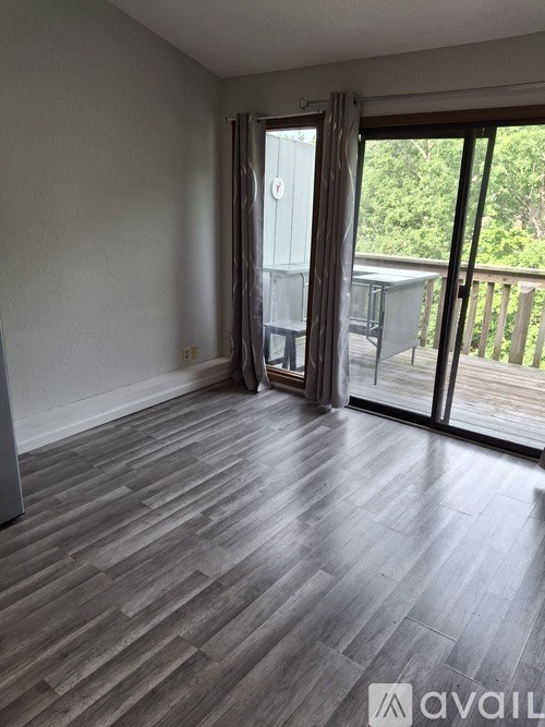 A room with wooden flooring and sliding glass doors leading to a balcony.
