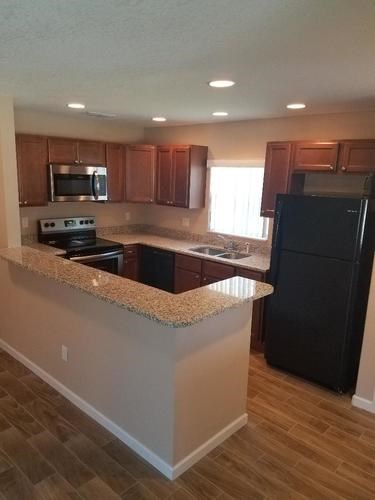 A kitchen with a black refrigerator and wooden cabinets.