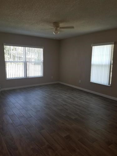 A room with wooden flooring and two windows.