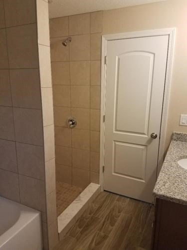 A white door is in a bathroom with a tiled shower area.