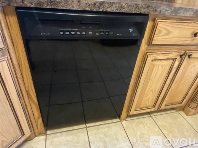 A black dishwasher is in a kitchen with wooden cabinets.