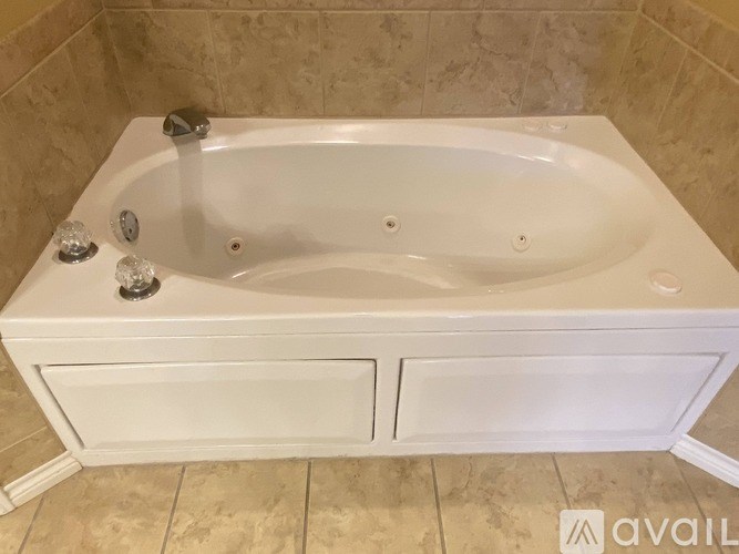 A white bathtub with a faucet and two handles is in a tiled bathroom.