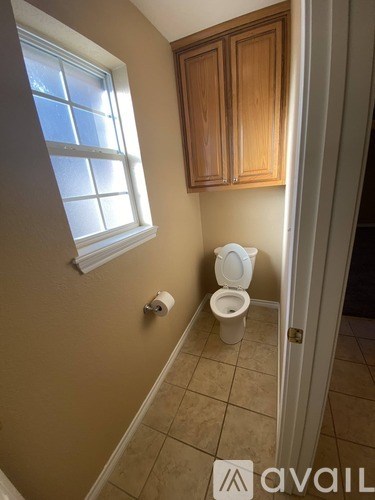 A bathroom with a toilet, a window, and wooden cabinets.