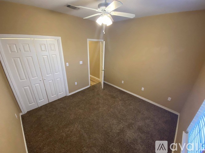 A room with a carpeted floor, a ceiling fan, and a door.