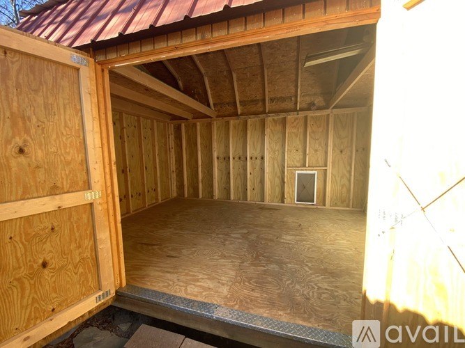 A wooden shed with a metal roof and a door open to the interior.