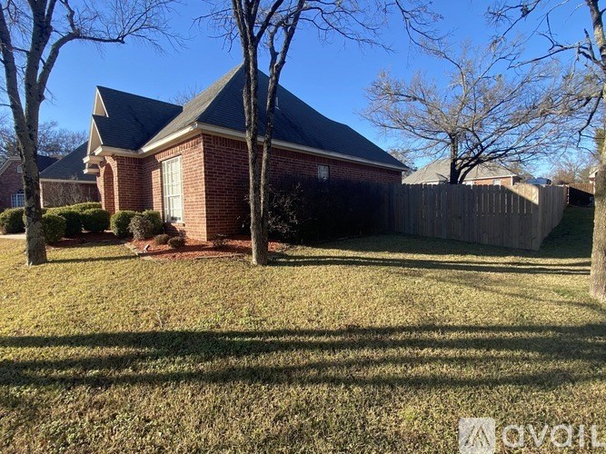 A house with a red brick exterior and a grey roof is surrounded by a wooden fence and leafless trees.