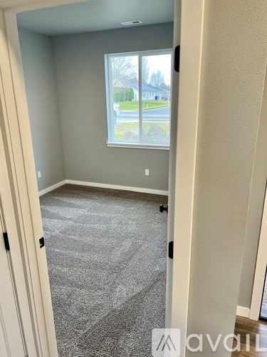 A room with a grey carpet and a window overlooking a street.