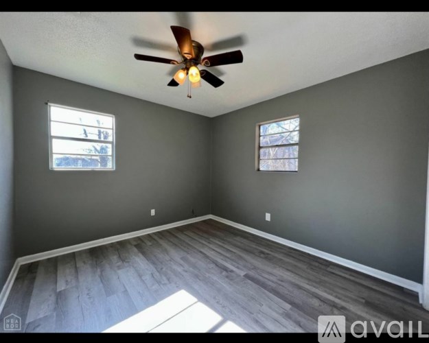 A room with a ceiling fan and two windows.