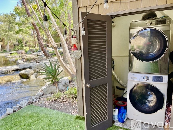 A washing machine is placed outside a house near a waterfall.