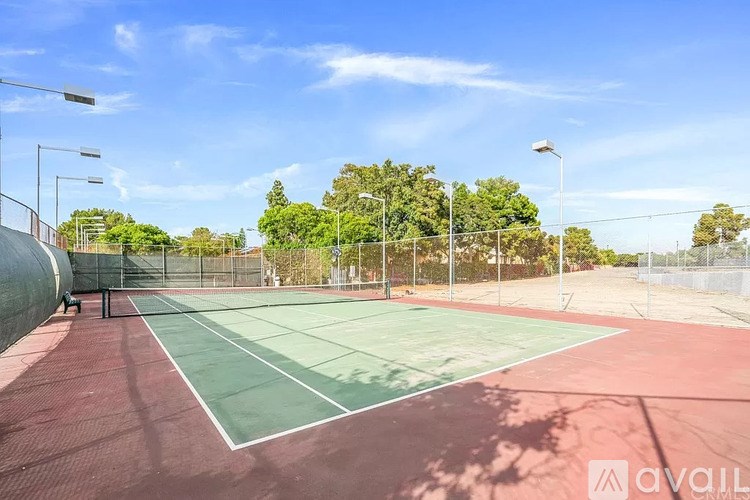 A tennis court with a green and red surface surrounded by a fence and trees.