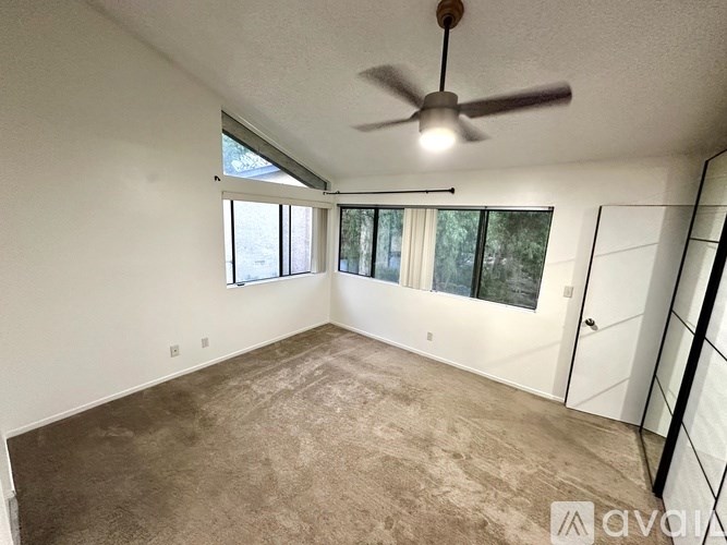 A room with a ceiling fan and a window with a view of trees.