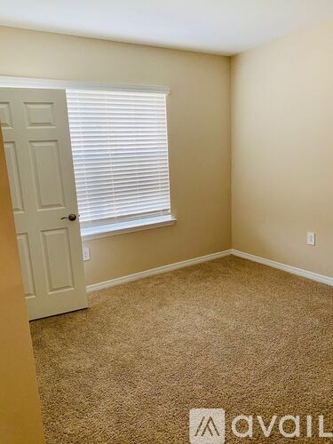 A room with a carpeted floor, a door, and a window with blinds.