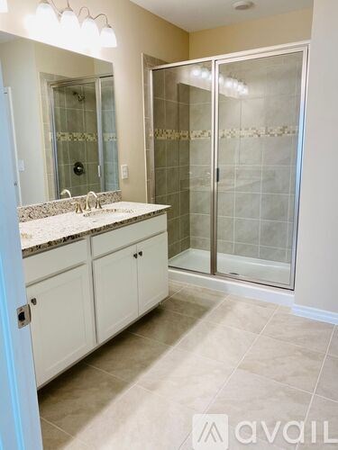 A bathroom with a glass shower door and a sink with a granite countertop.