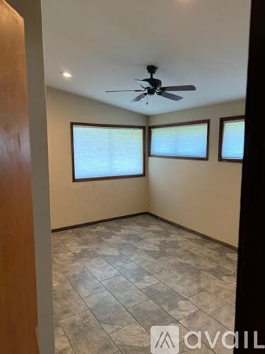 A room with a ceiling fan and two windows.