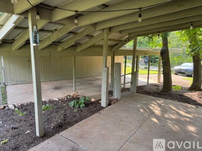 A covered patio area with a concrete floor and a roof supported by wooden beams.