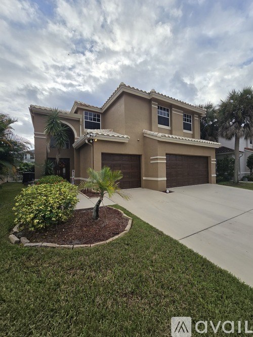 A house with a brown roof and tan walls is surrounded by a well-manicured lawn and a clear sky.