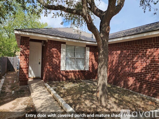 A red brick house with a covered porch and a mature shade tree in front.