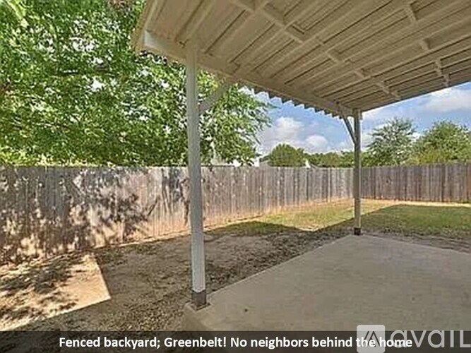 A backyard with a fence and a greenbelt behind it.