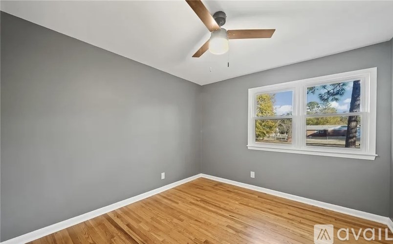 A room with a ceiling fan and a window showing a view of trees and a building outside.