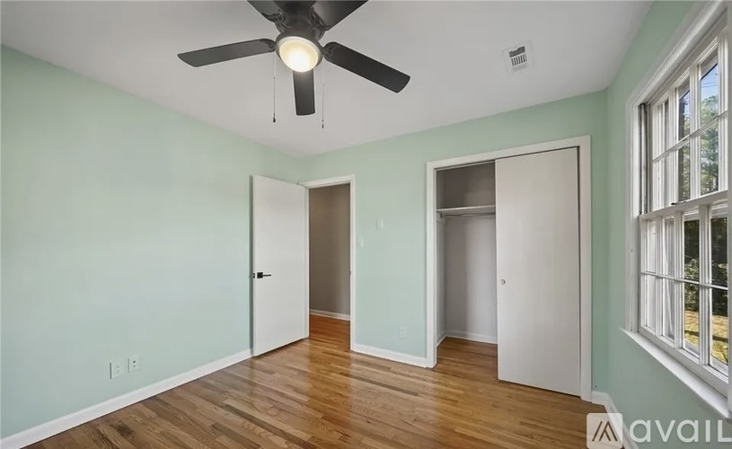 A room with a ceiling fan and light, hardwood floors, and two doors leading to other rooms.
