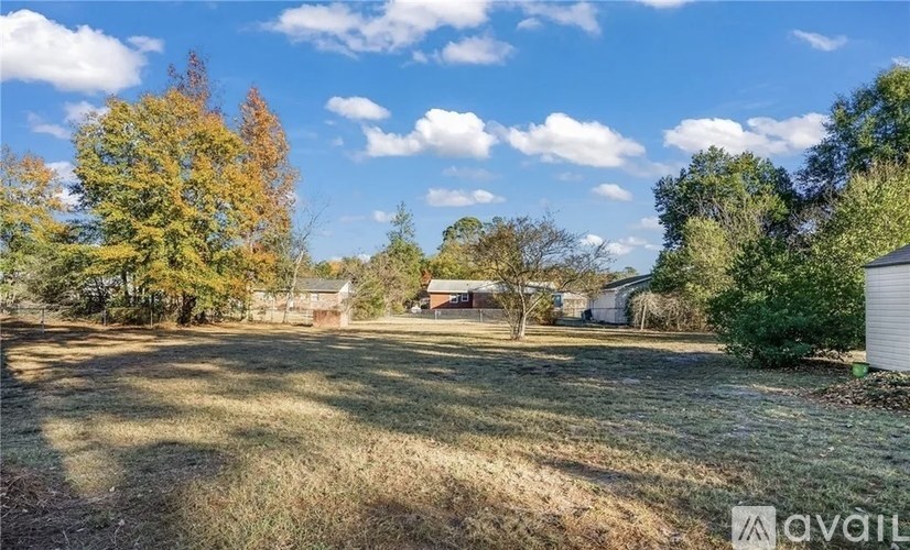 A field with trees and a house in the background.