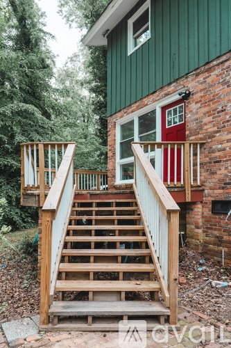 A wooden staircase leads up to a green building with a red door.