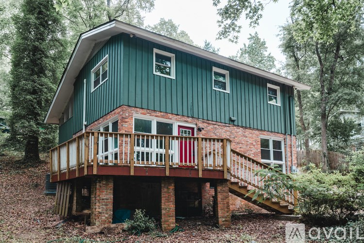 A green house with a red door and a wooden deck.