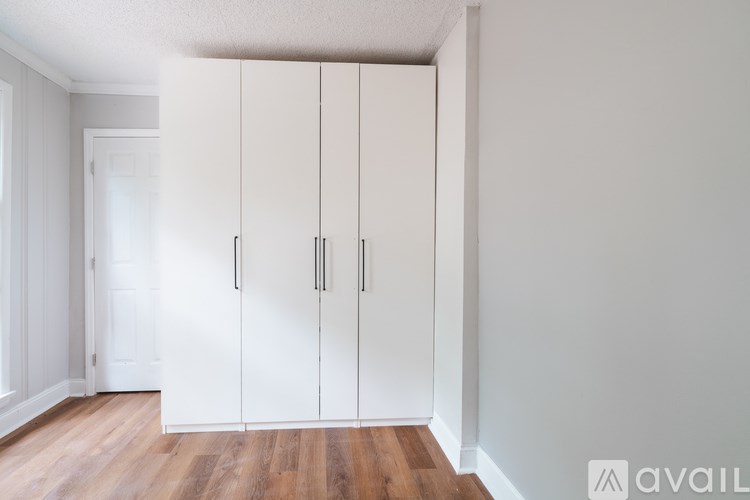 A room with a set of white cupboards and wooden flooring.
