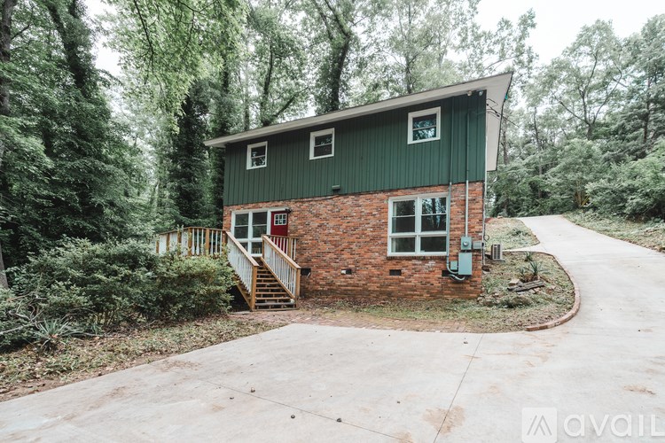 A house with a green roof and a brick chimney is surrounded by trees.