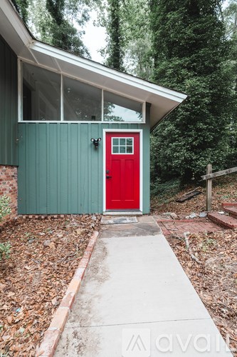 A small house with a red door is surrounded by trees.