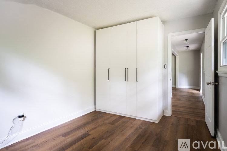 A room with white walls and wooden flooring, featuring a set of white cabinets with black handles.