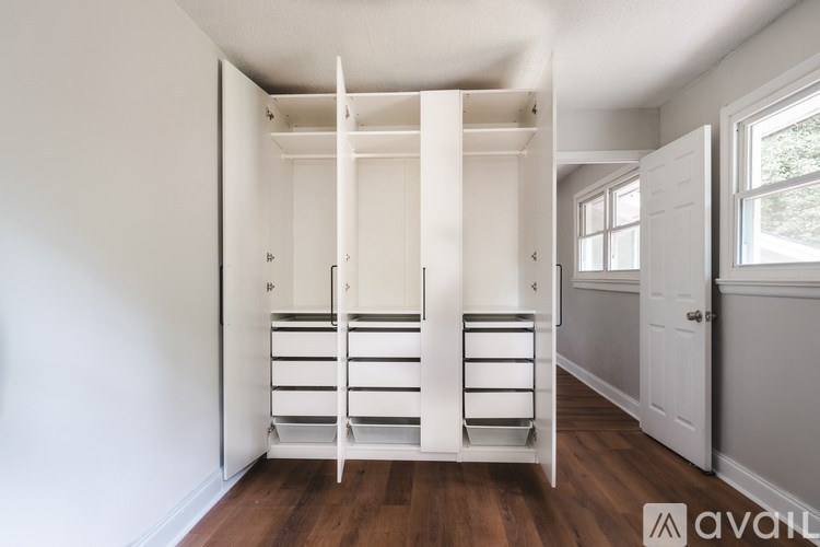 A white closet with shelves and drawers is in a room with wood floors and white walls.