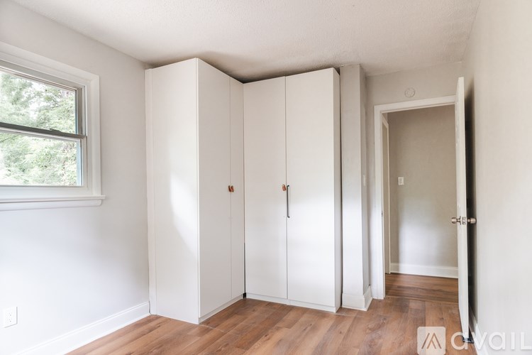 A room with white walls and wooden floors has a window and a set of white closet doors.