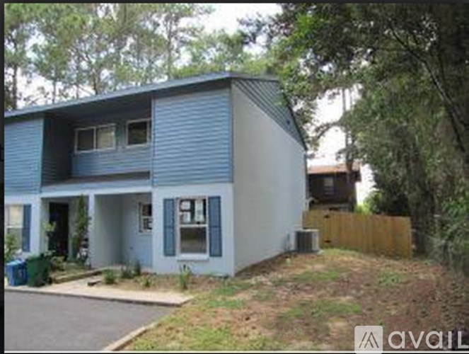 A blue house with a white door and windows is surrounded by trees.
