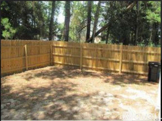 A backyard with a wooden fence and a trash can.